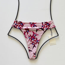 Flat lay of Acacia Swimwear Mateo bikini bottom in Mokoli’i, a pink base with red, purple, and blue tropical floral print, featuring a fold-over waistband and high-cut design.