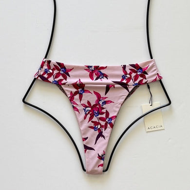 Flat lay of Acacia Swimwear Mateo bikini bottom in Mokoli’i, a pink base with red, purple, and blue tropical floral print, featuring a fold-over waistband and high-cut design.