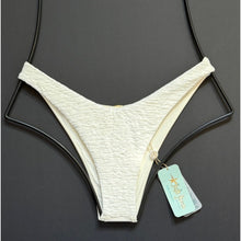 Ivory textured high-leg Brazilian bikini bottom by Luli Fama with gold charm detail, displayed flat with original tags.