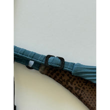 Close-up of Acacia Swimwear Ralphy Bikini Bottom in Horizon, showing matte logo hardware engraved with “ACACIA” and adjustable side strap detail over ribbed tan fabric with subtle animal-print lining beneath.