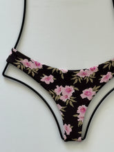 Close-up of Acacia Ho’okipa bikini bottom in Floret print. Dark brown background with pink flowers and olive leaves, low-rise cheeky fit.
