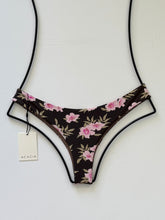 Acacia Ho’okipa bikini bottom in Floret floral print, front angle. Minimal coverage Brazilian cut in black with pink flower detailing