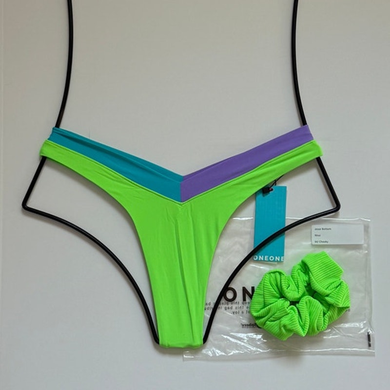OneOne Swimwear Jesse Bikini Bottom in Nissi Neon Green with aqua and lilac V-shaped waistband, size medium, flat lay with matching scrunchie on white background